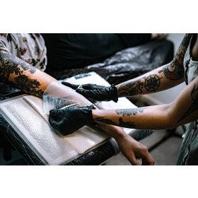 studiofoto, tätowierer bringt den tattoomed protection uv film auf der frischen Tätowierung am Kunden an